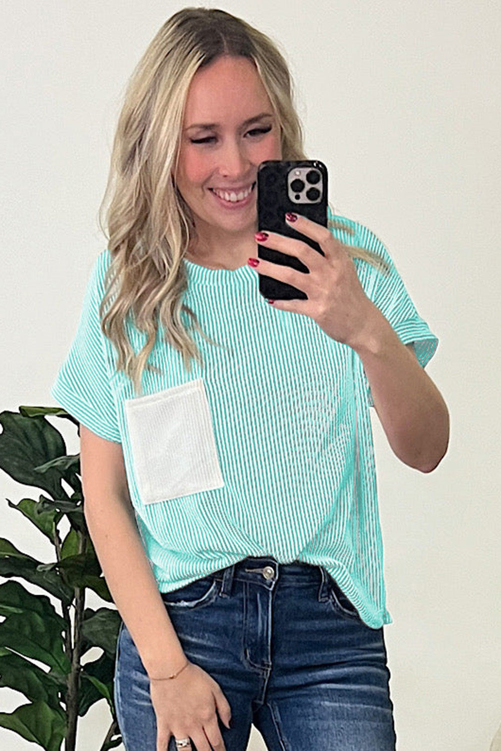 Woman taking a mirror selfie wearing a light blue striped shirt with a pocket and blue jeans.