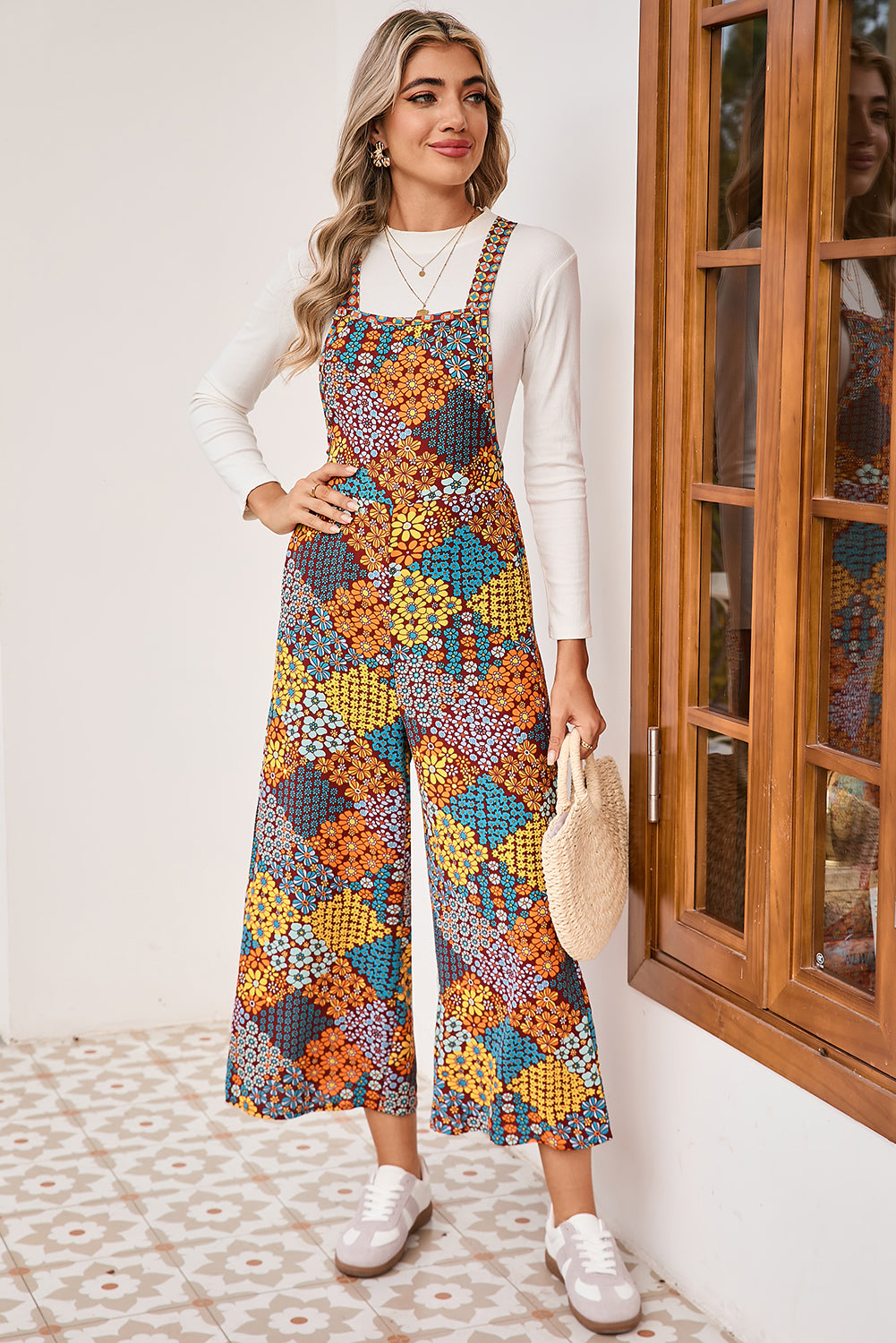 Woman wearing a colorful floral overalls standing in a room with wooden window frames.