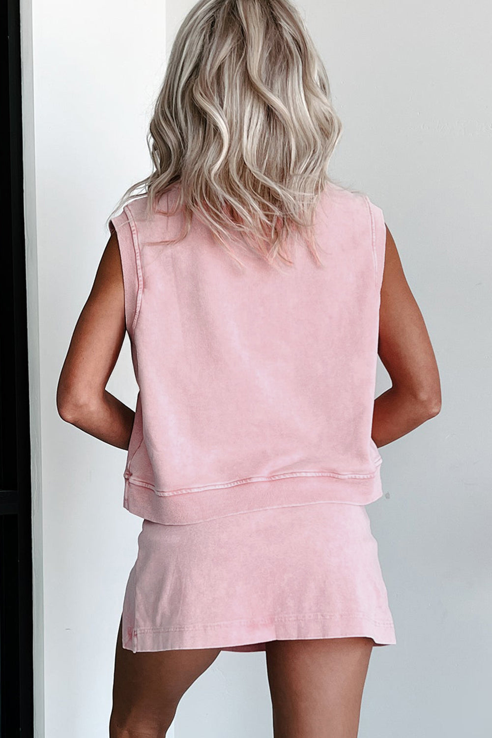 Person wearing a pink sleeveless top and skirt set against a white background