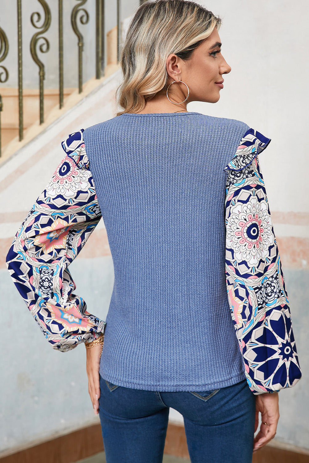 Woman wearing a blue ribbed sweater with patterned sleeves against a neutral background