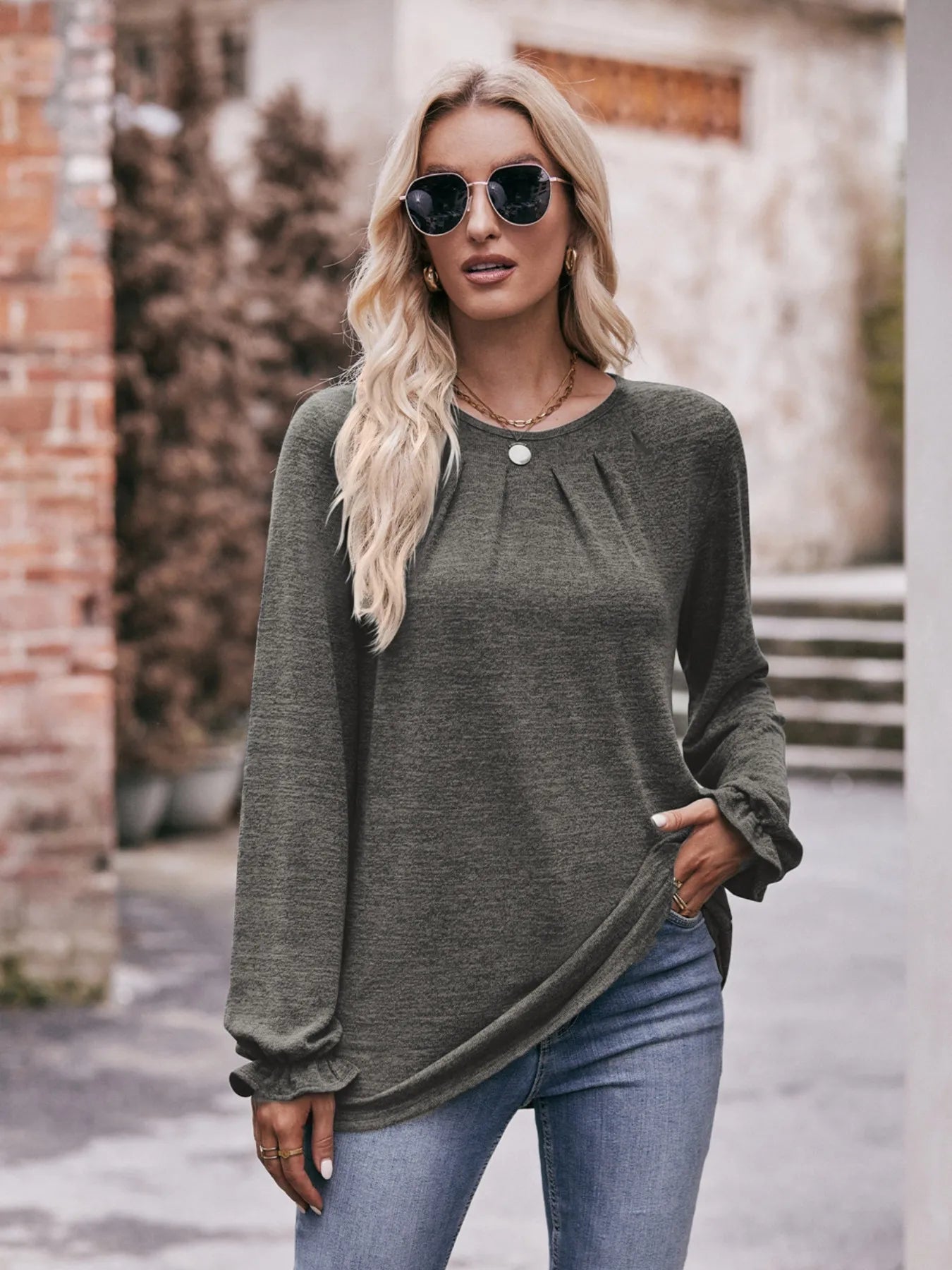 Woman wearing a green sweater and blue jeans outdoors.