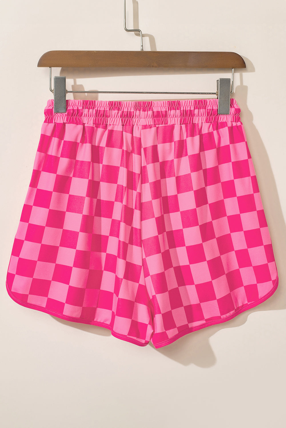 Pink checkered shorts on a hanger against a beige background