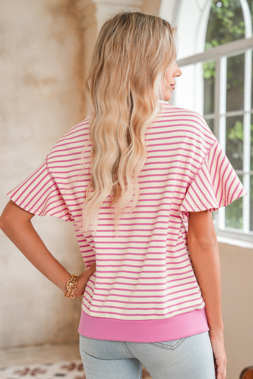 Woman wearing a pink and white striped shirt in a room with a window.