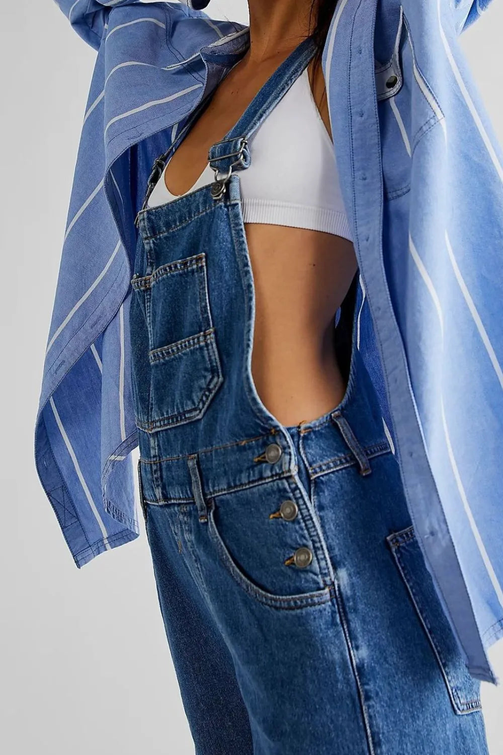 Person wearing a blue denim jacket and overalls on a plain background
