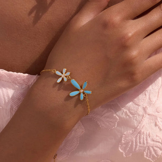 Gold bracelet with blue flower charms on a wrist against a pink textured background