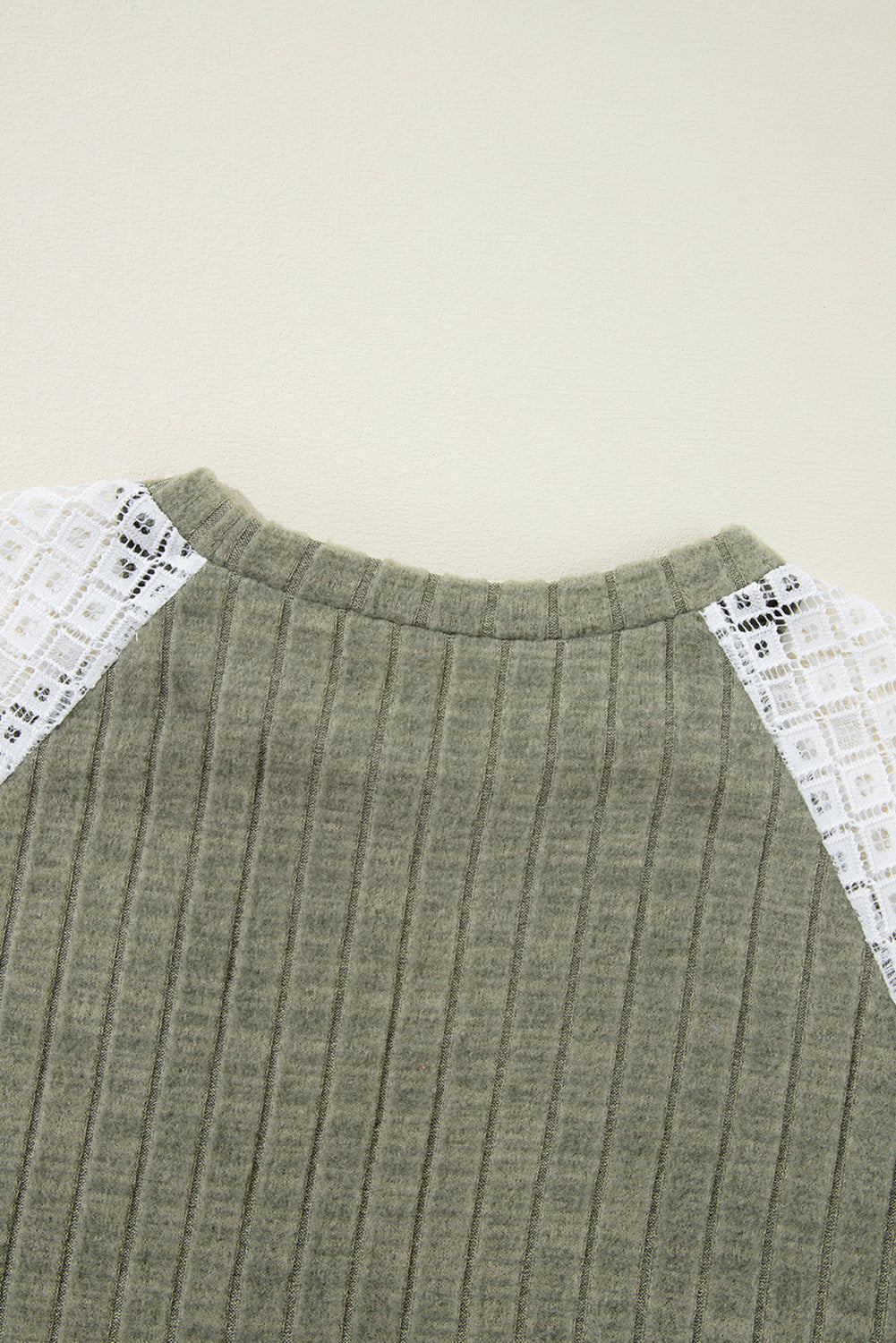 Green ribbed sweater with white lace sleeves on a beige background