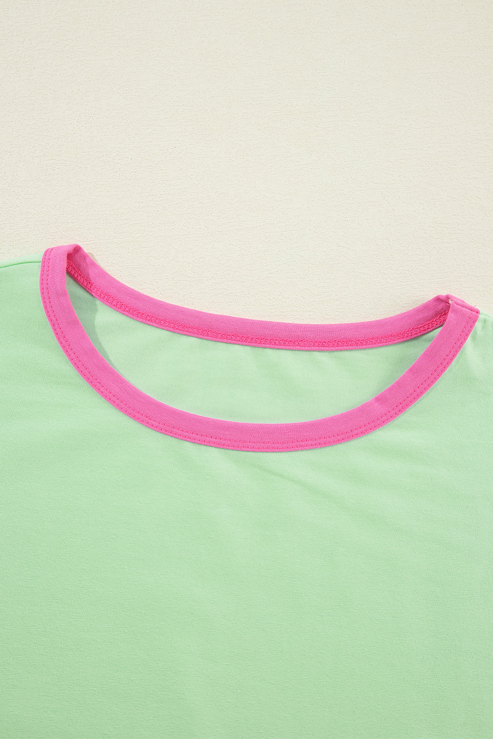 Close-up of a green shirt with pink neckline on a beige background
