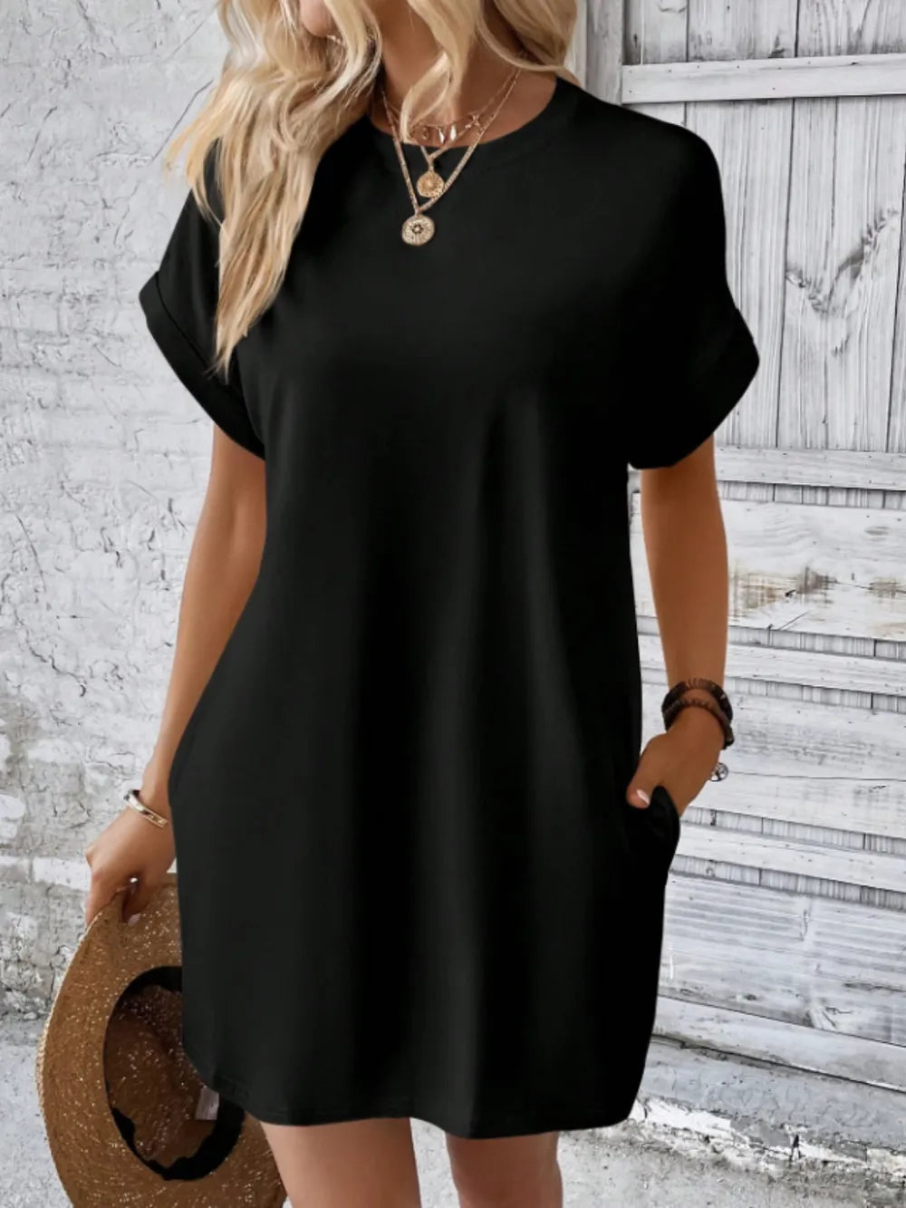 Woman wearing a black dress holding a hat against a wooden background