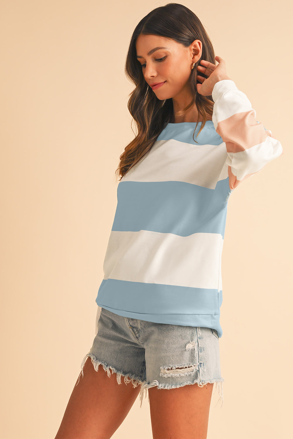 Woman wearing a striped sweater and denim shorts on a beige background