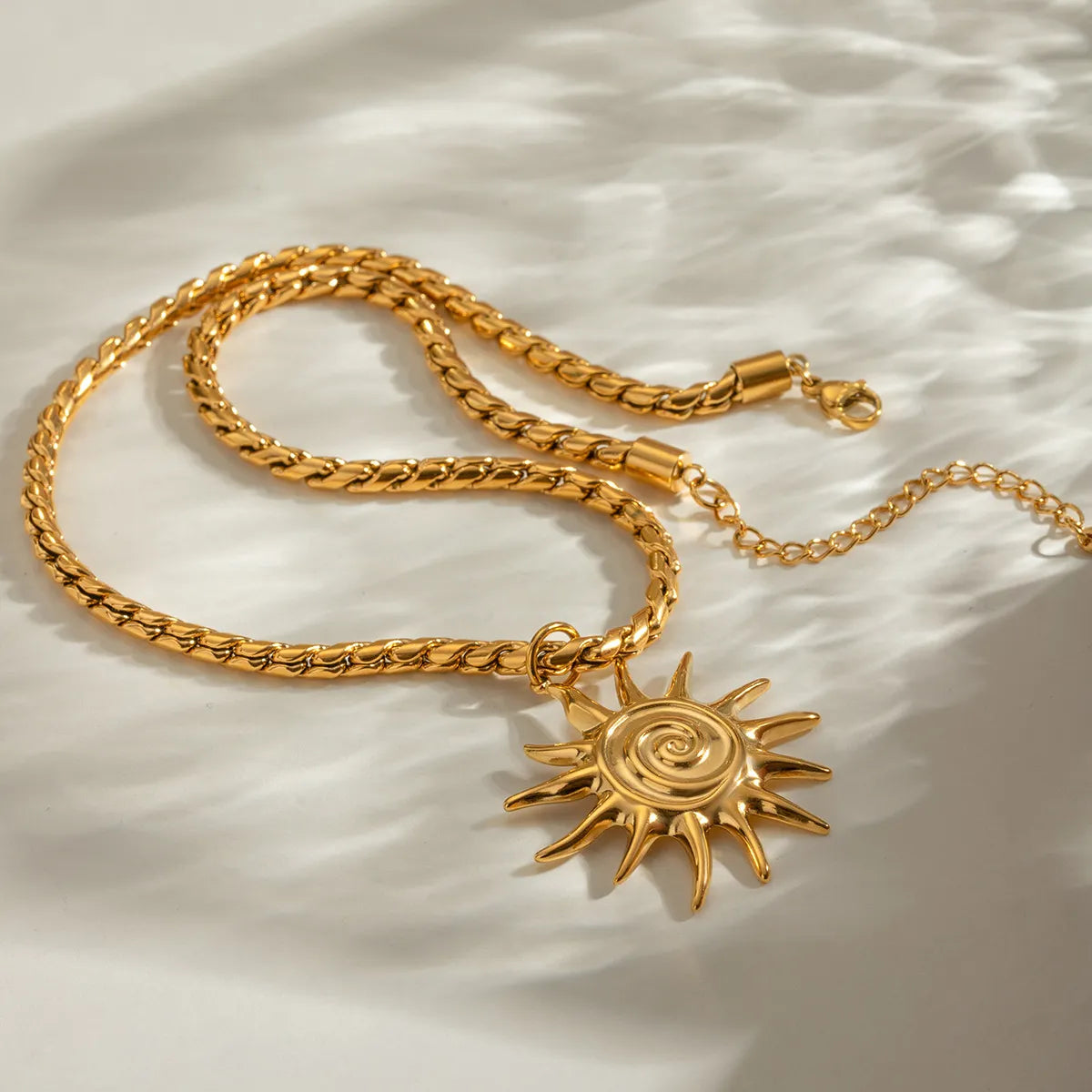 Gold chain necklace with a sun-shaped pendant on a light fabric background