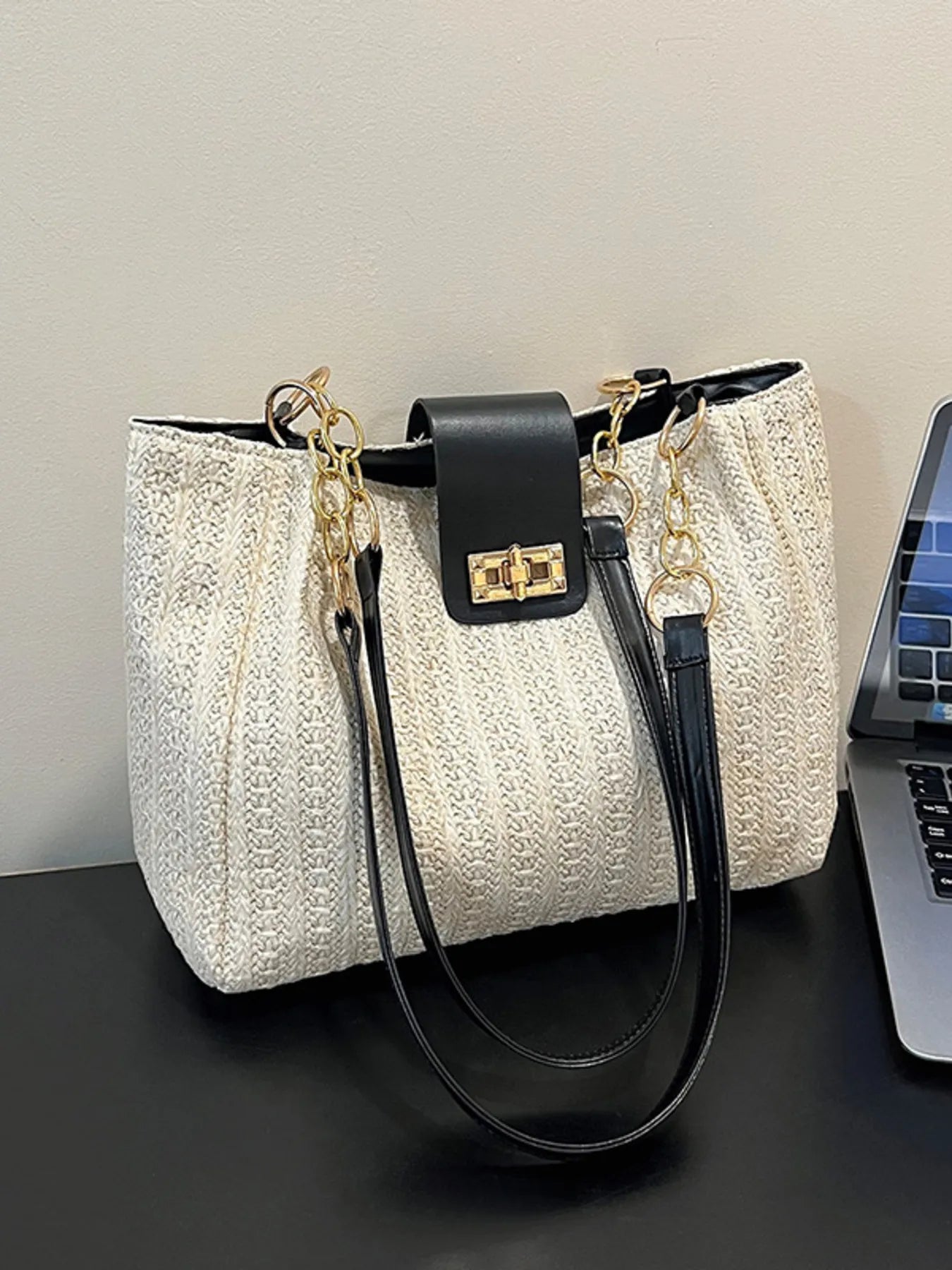 White textured handbag with black handles and gold accents on a dark surface.