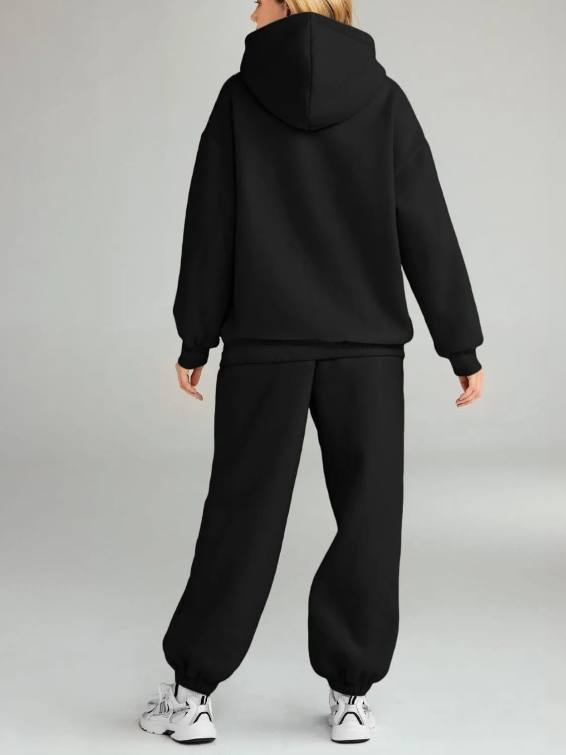 Person wearing a black hoodie and black pants on a gray background