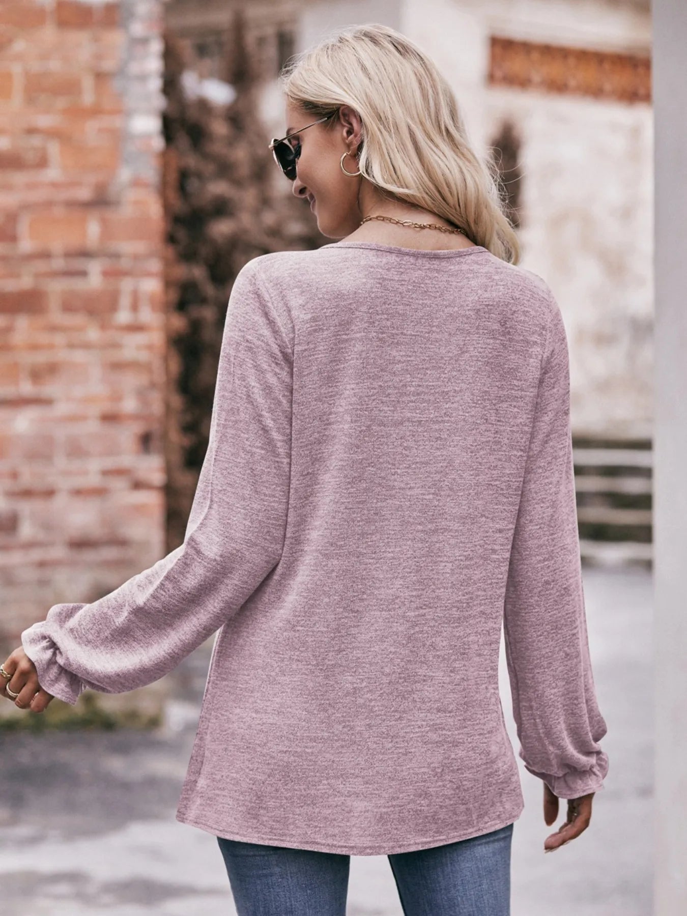 Woman wearing a pink sweater and sunglasses, standing outdoors.