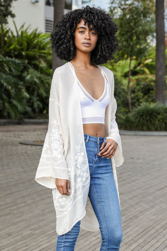 Woman wearing a white lace kimono over a white top and blue jeans outdoors.