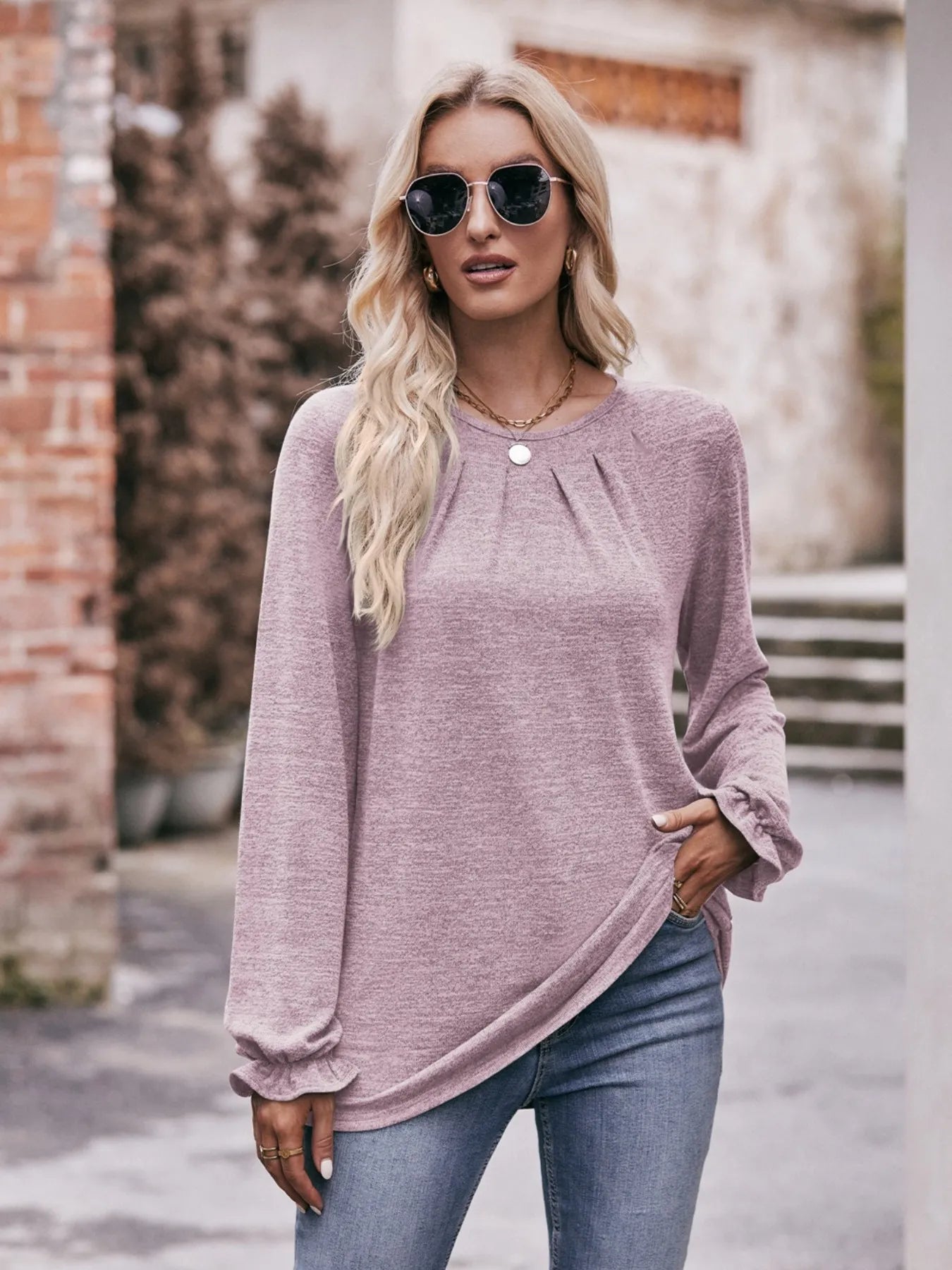 Woman wearing a light purple long-sleeve top and blue jeans outdoors.
