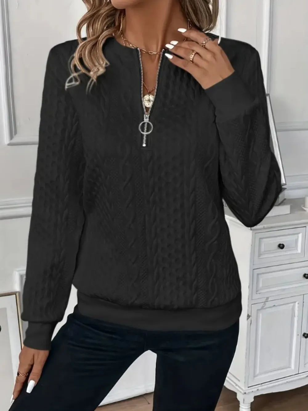 Person wearing a black textured sweater with a zipper in a room with white cabinets.