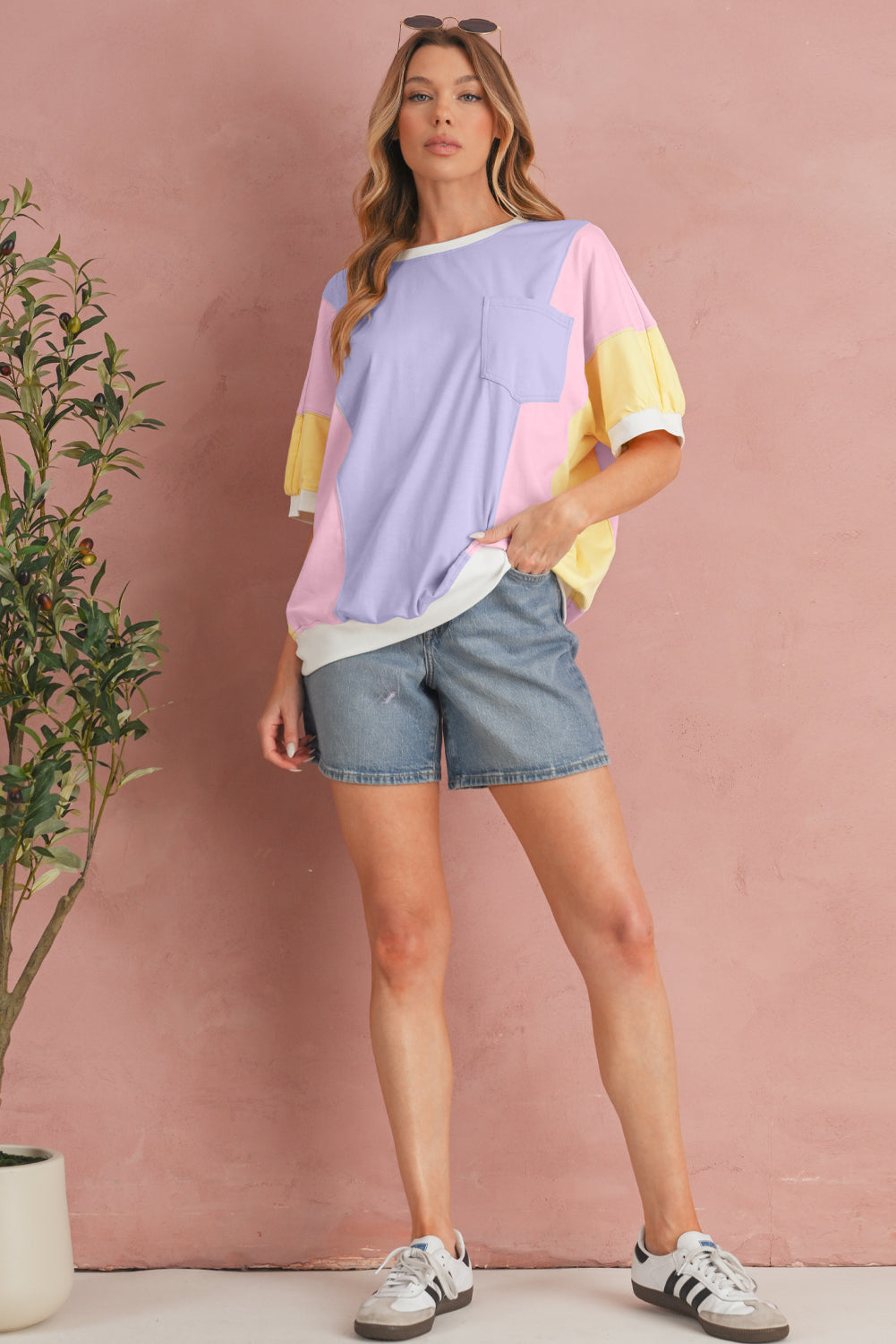 Woman wearing a colorful top and denim shorts against a pink wall.