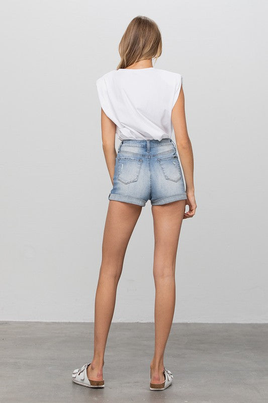 Woman wearing denim shorts and a white top on a plain background