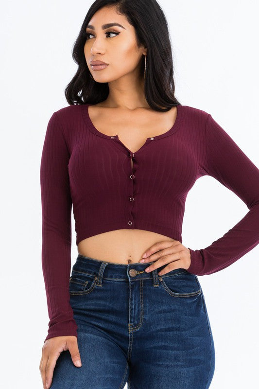 Woman wearing a burgundy long-sleeve crop top and blue jeans on a white background