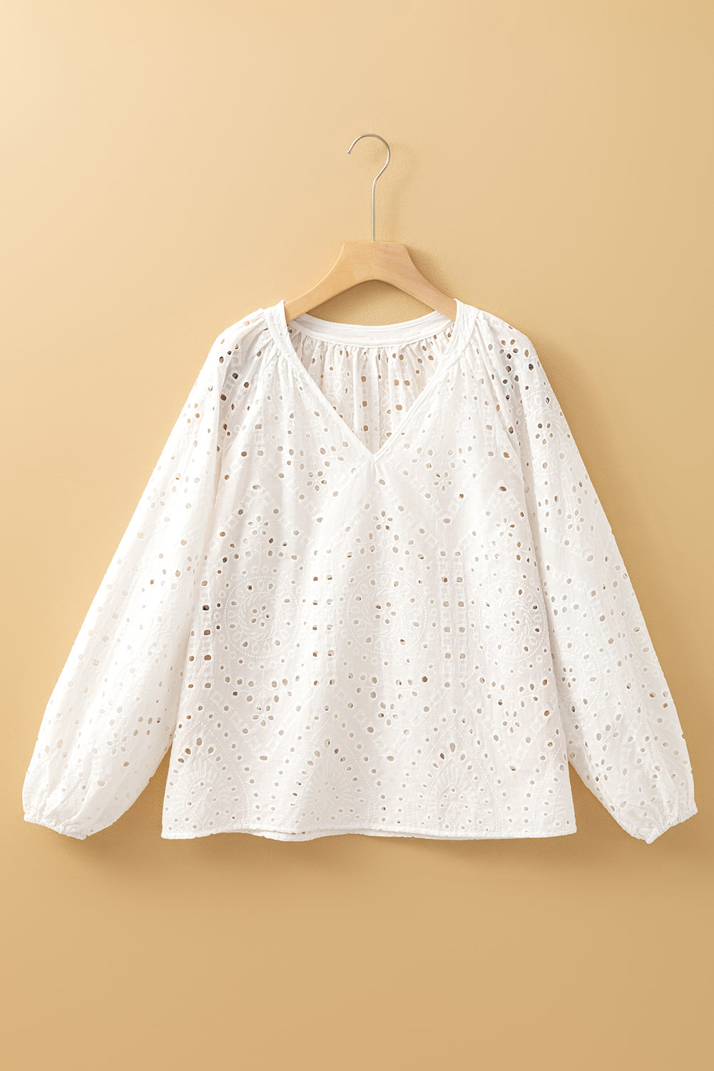 White blouse with long sleeves on a hanger against a beige background