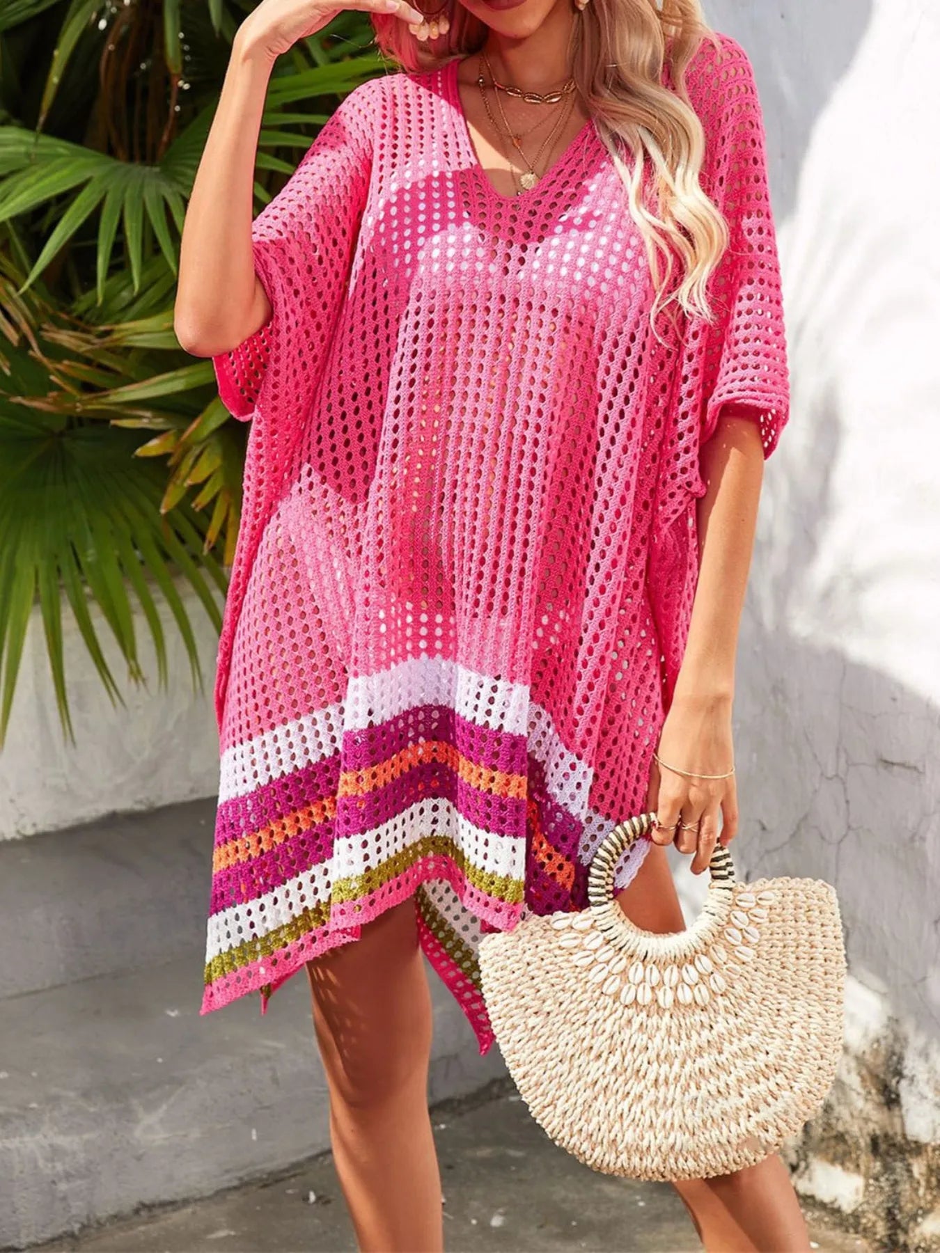 Woman wearing a pink crochet cover-up with a straw bag against a tropical background