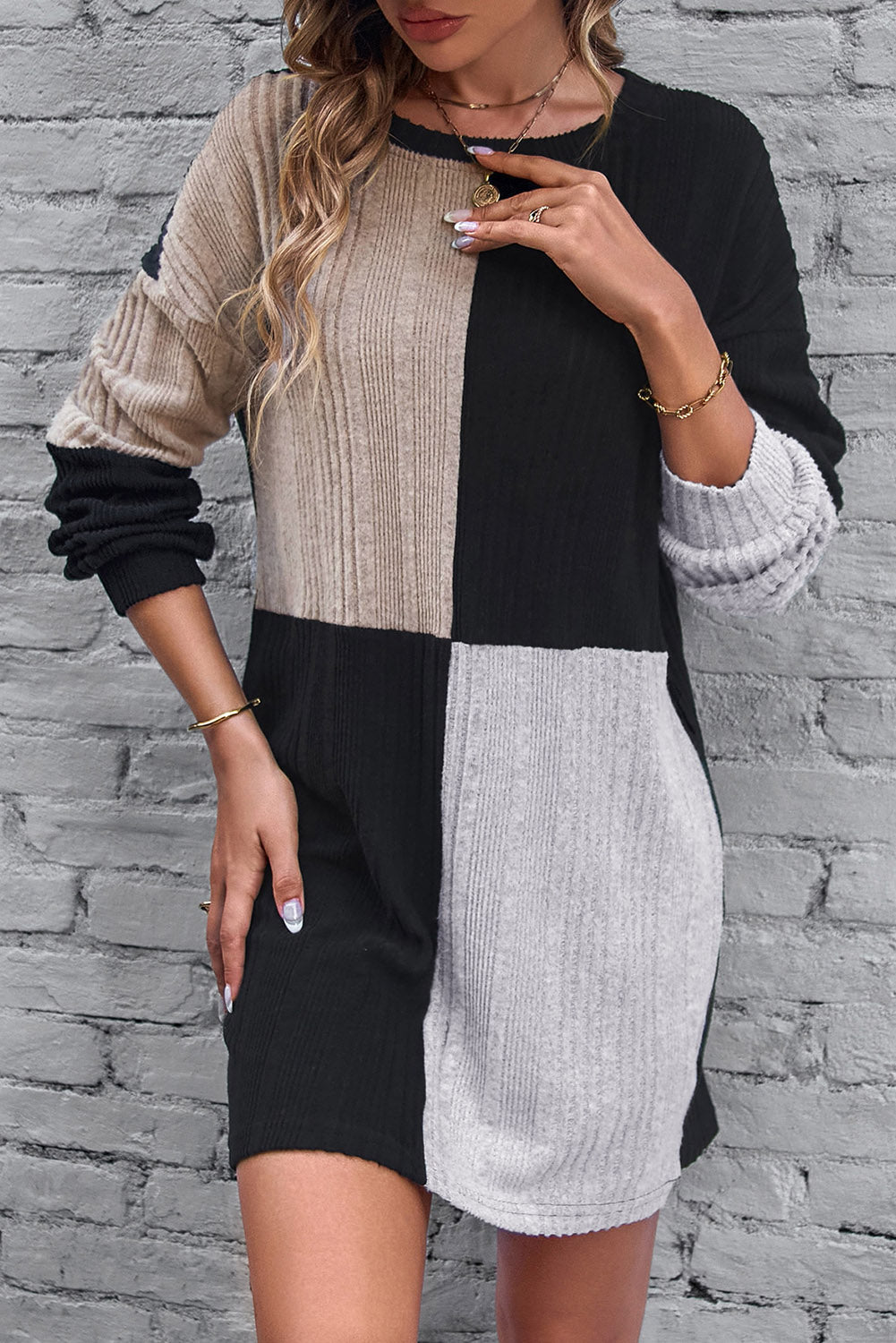 Woman wearing a black, beige, and gray color-blocked dress against a brick wall.
