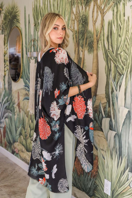 Woman wearing a black floral kimono in front of a nature-themed wall.