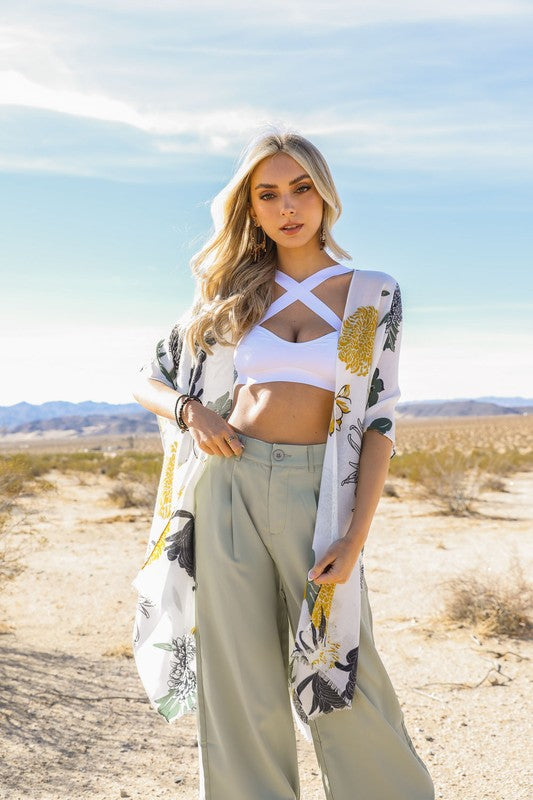 Woman in a desert setting wearing a white crop top and light-colored pants with a floral kimono.