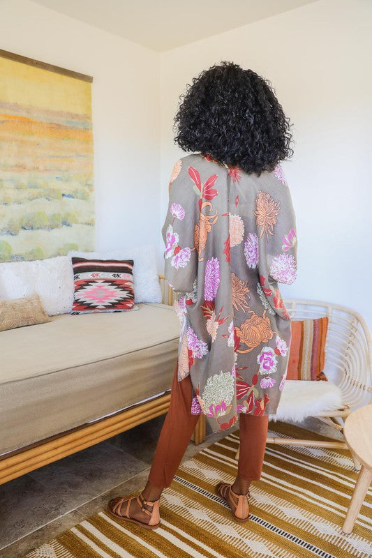 Woman in a floral kimono standing in a living room with a couch and colorful rug.