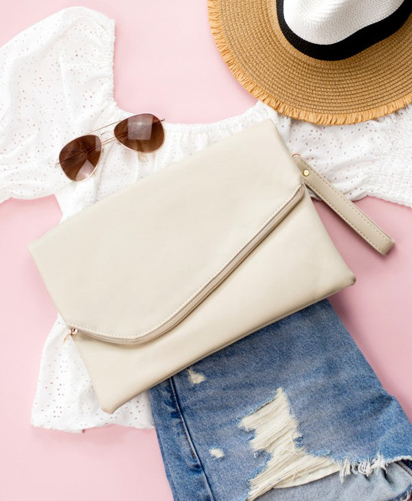 Beige clutch bag, sunglasses, white lace top, and denim shorts on a pink surface