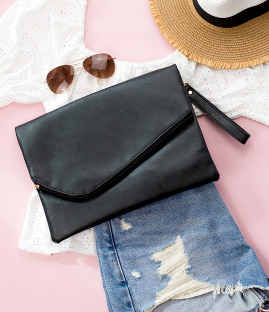 Black clutch bag on denim jeans with sunglasses and a hat on a pink surface