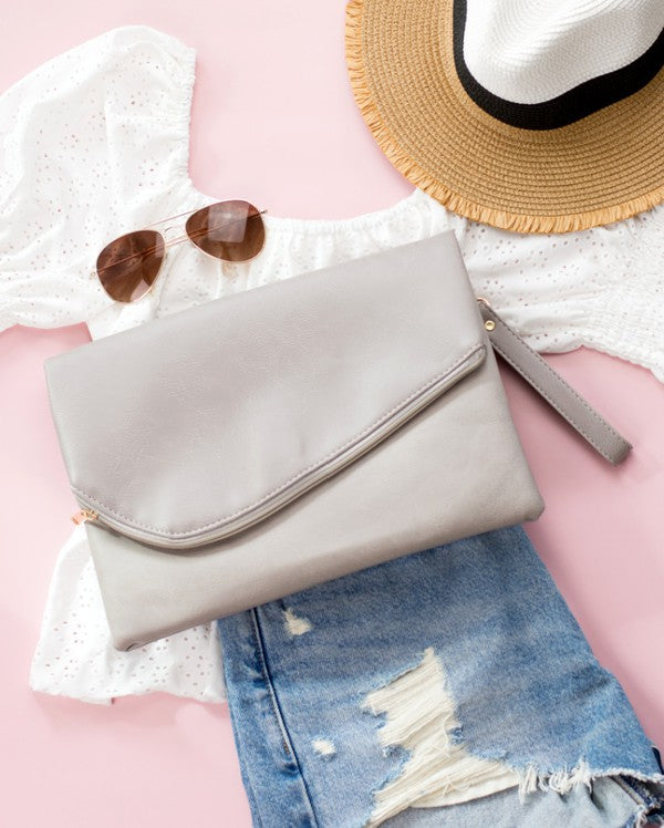 Light gray clutch bag with sunglasses, straw hat, and denim jeans on a pink surface