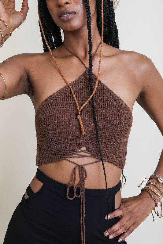 Woman wearing a brown knitted halter top and black pants against a plain background