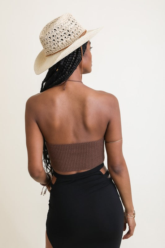 Person wearing a straw hat and black skirt with a neutral background