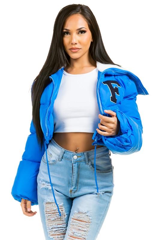 Woman wearing a blue jacket with a logo, white crop top, and ripped jeans on a white background