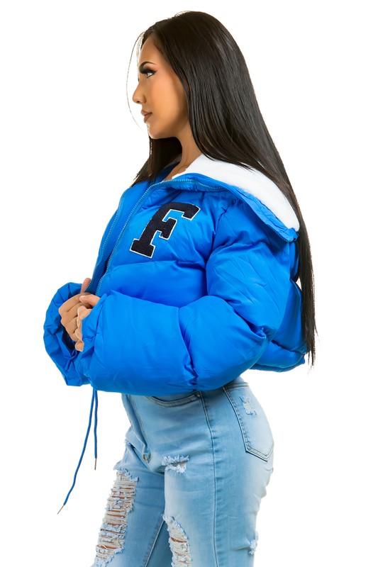 Woman wearing a blue puffer jacket with a letter 'F' on a white background