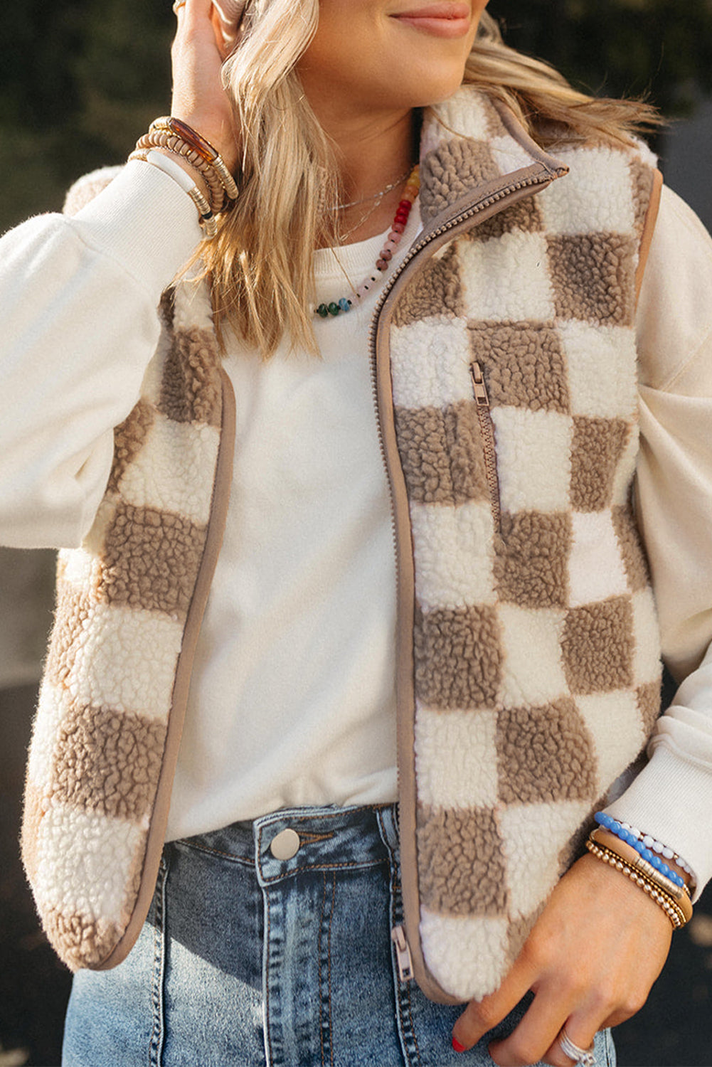 Person wearing a checkered fleece vest over a white shirt with denim jeans.