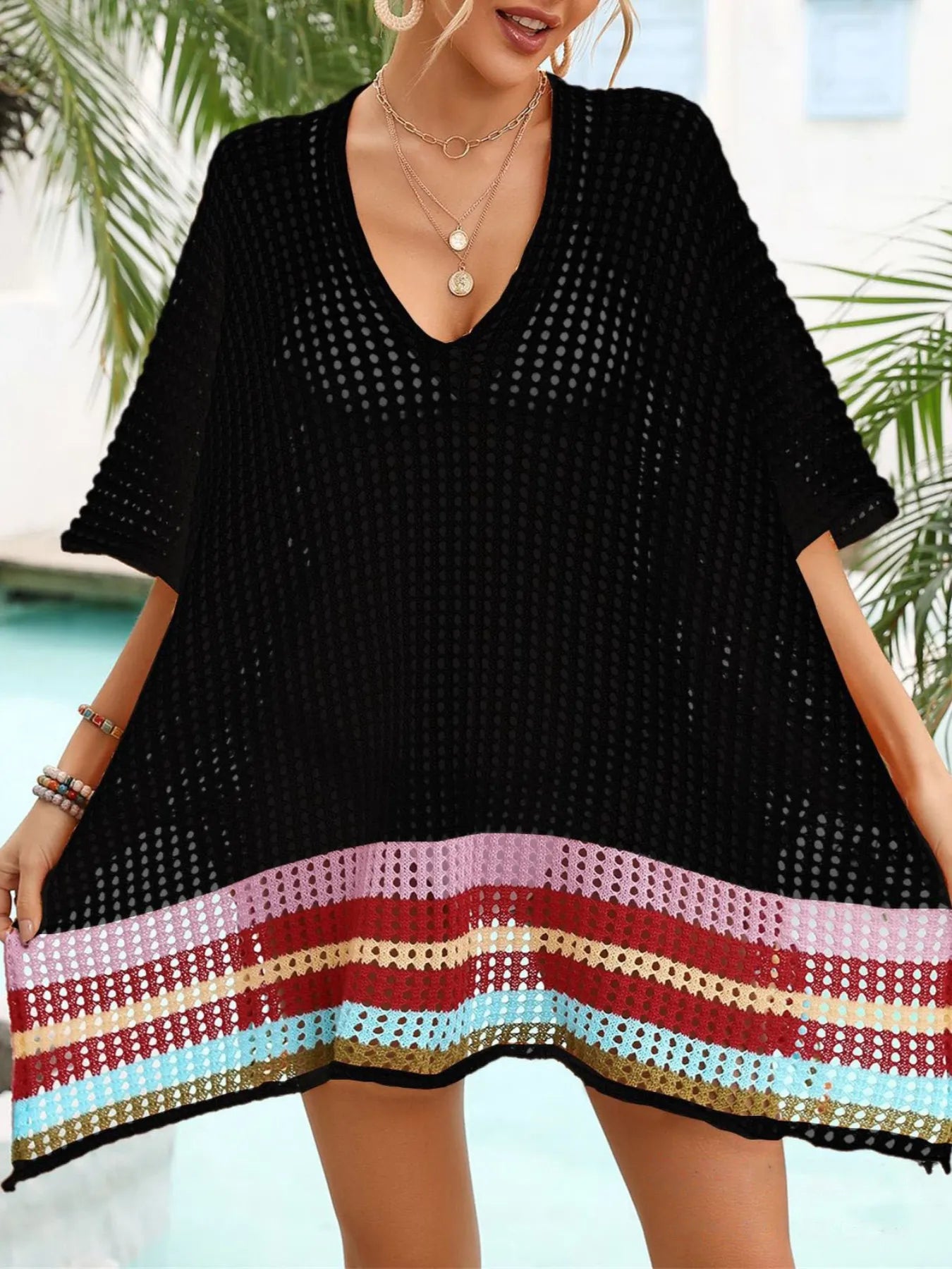 Woman wearing a black crochet cover-up with colorful trim by a poolside.