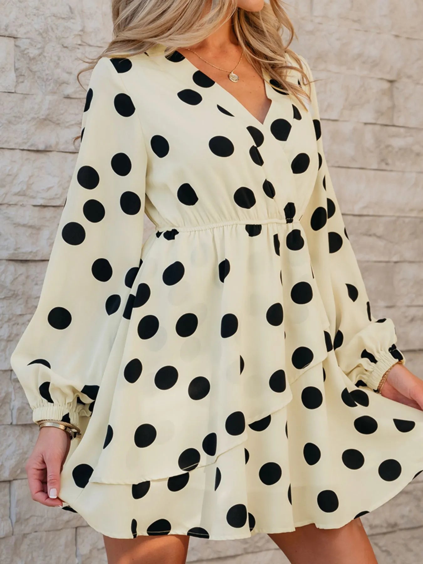 Woman wearing a polka dot dress with long sleeves against a stone wall.