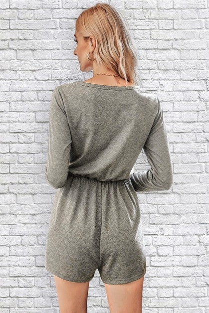 Woman wearing a gray romper against a white brick wall