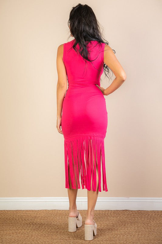 Woman wearing a bright pink dress with fringe details, standing against a beige wall.