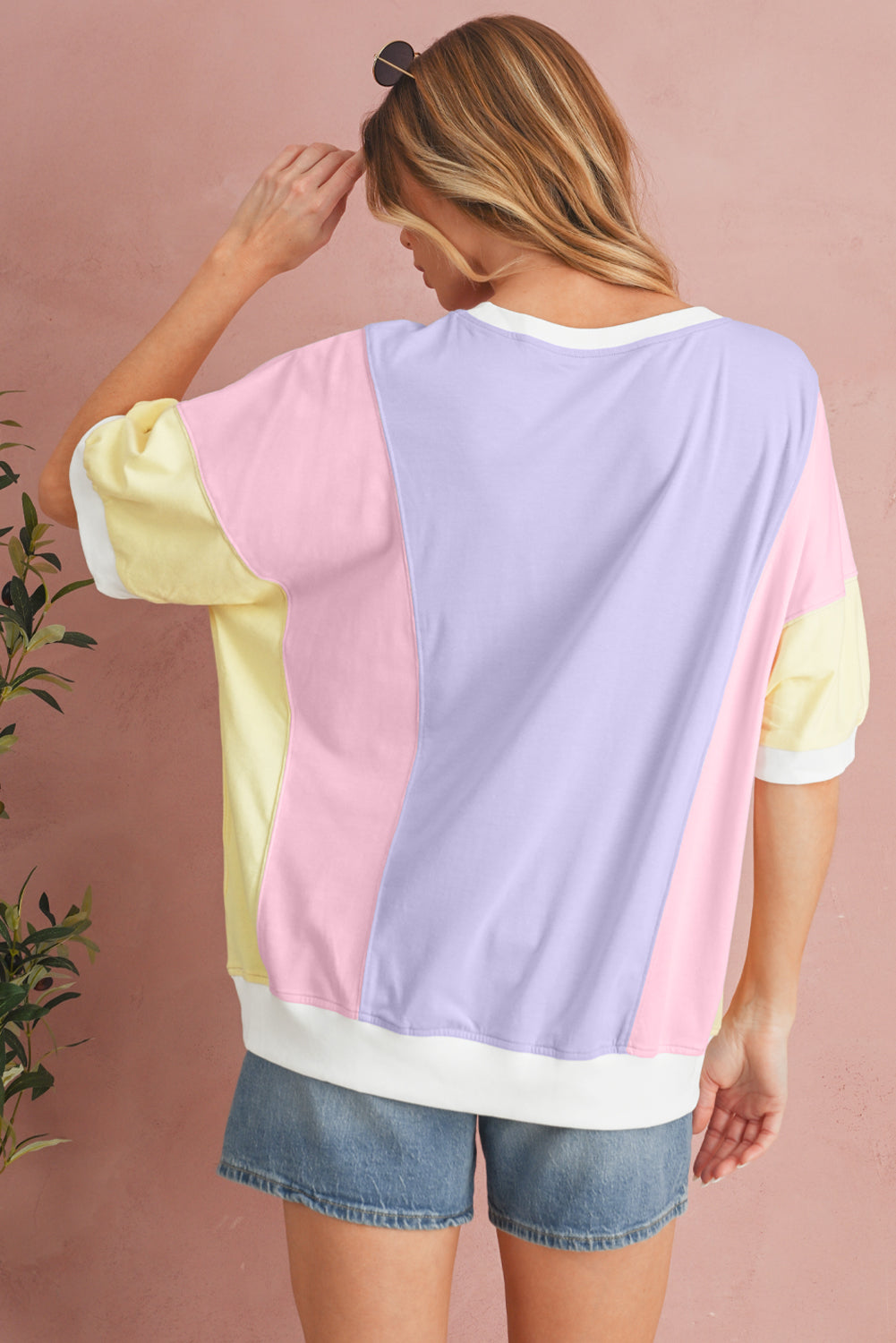 Woman wearing a colorful oversized shirt with a pink, yellow, and lavender design against a pink background.