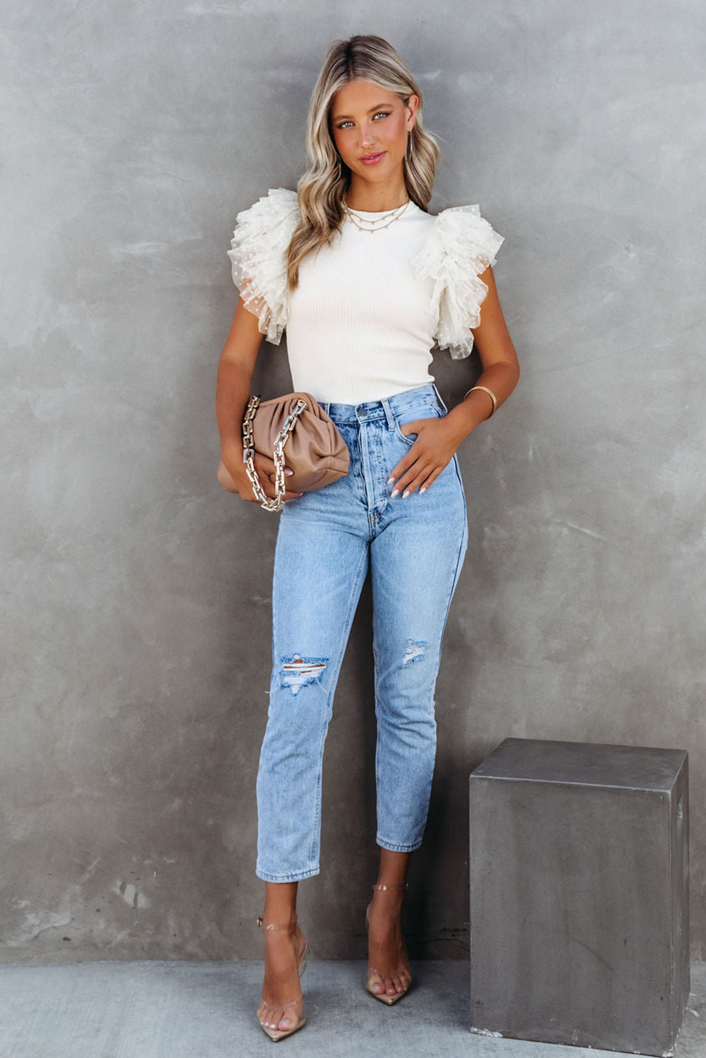 Woman wearing a white ruffled top and blue jeans against a gray background