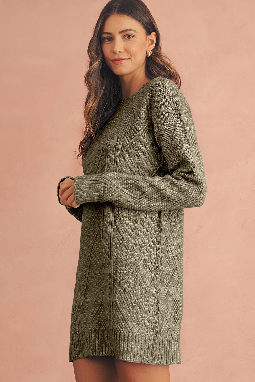Woman wearing a green cable knit sweater dress against a pink background