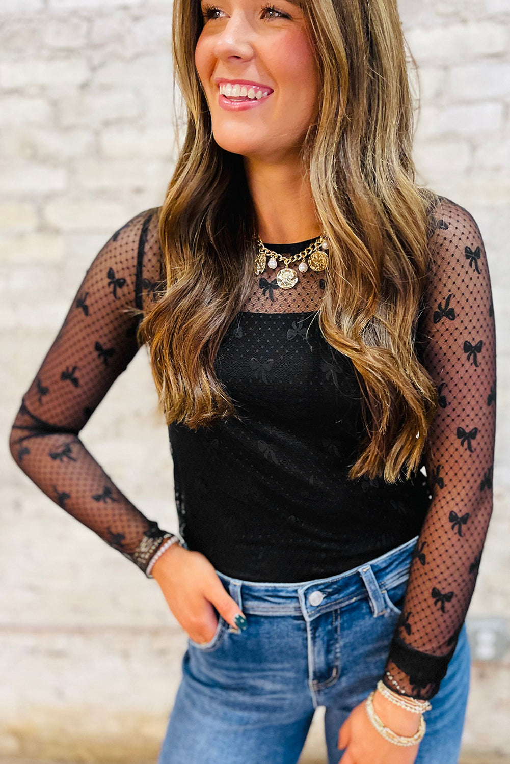 Woman wearing a black top with fishnet sleeves featuring black bow patterns, paired with blue jeans.