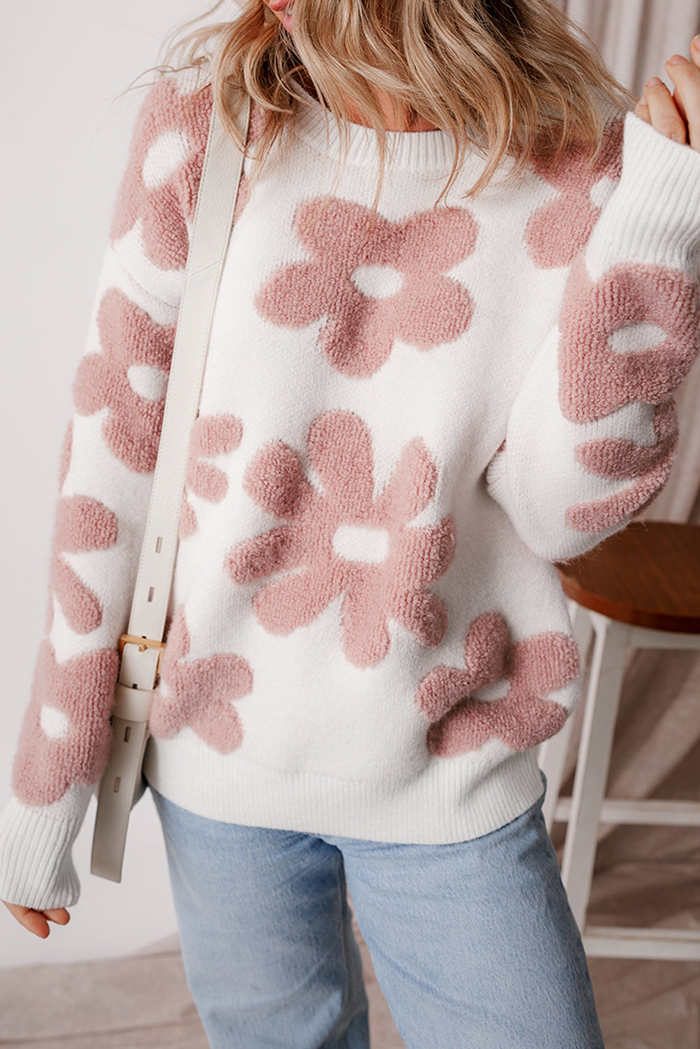 White sweater with pink floral patterns worn by a person indoors.