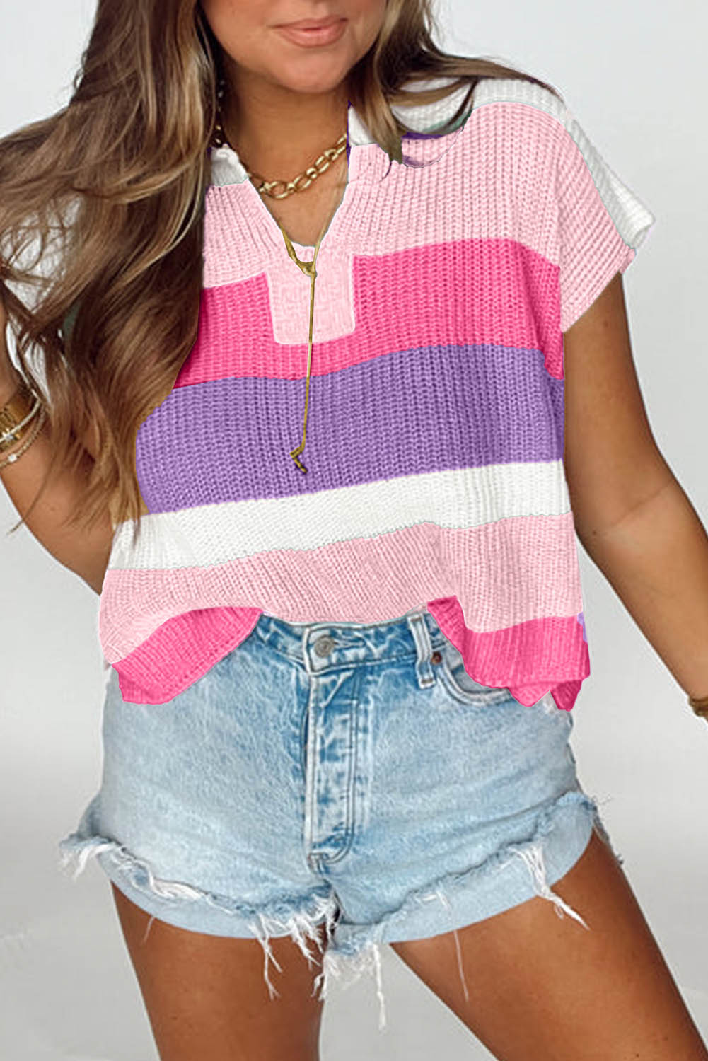 Woman wearing a colorful striped sweater and denim shorts on a plain background