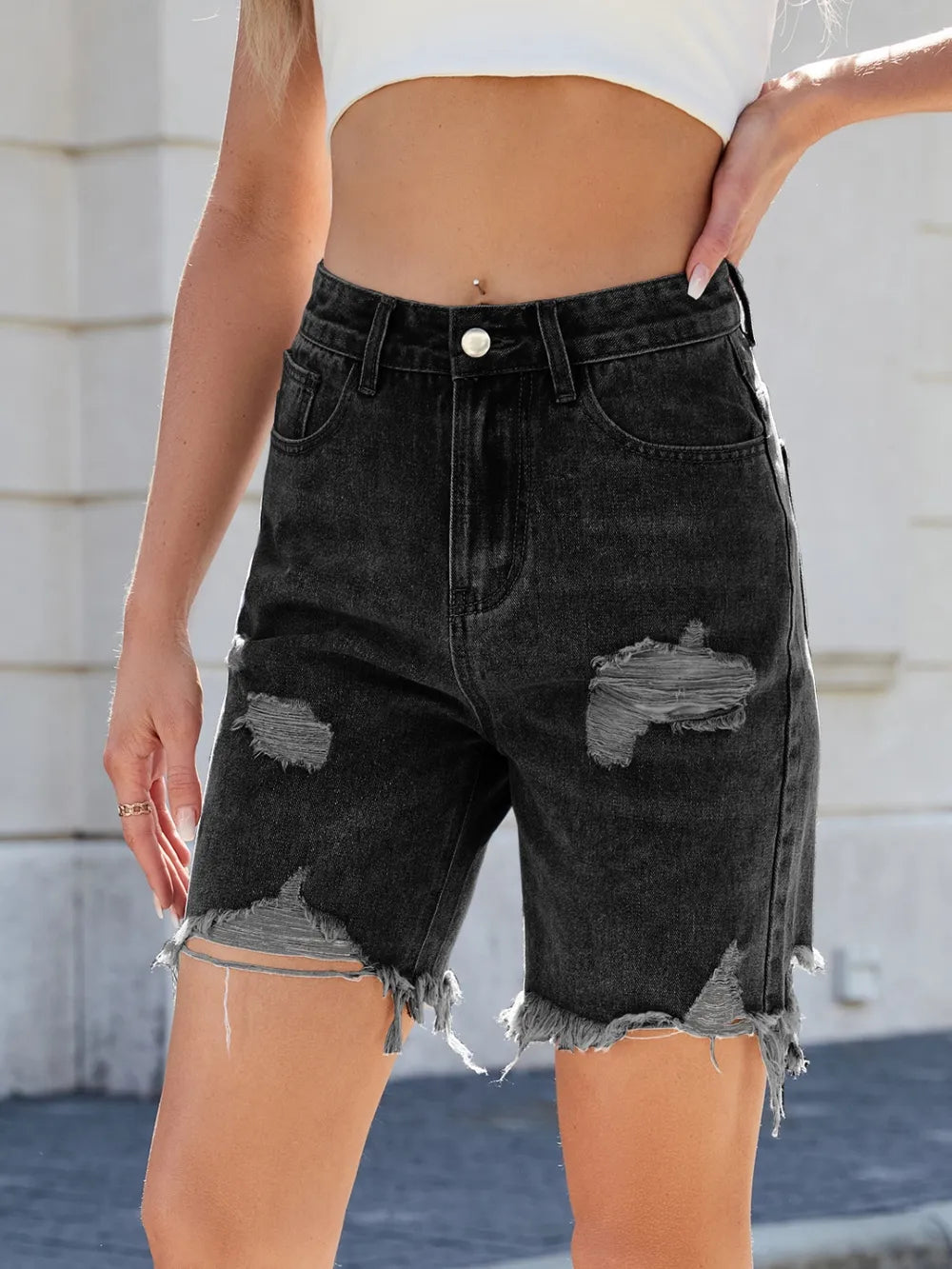 Black distressed denim shorts worn by a person with a blurred background