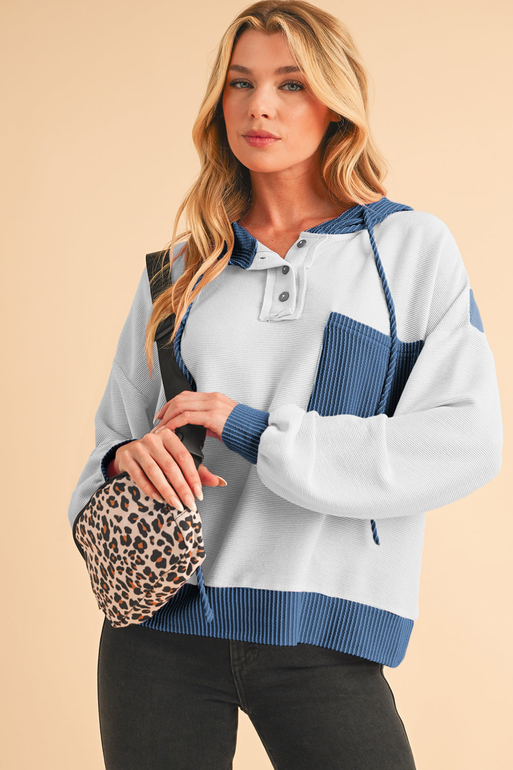 Woman wearing a blue and gray sweater with a leopard print bag on a beige background