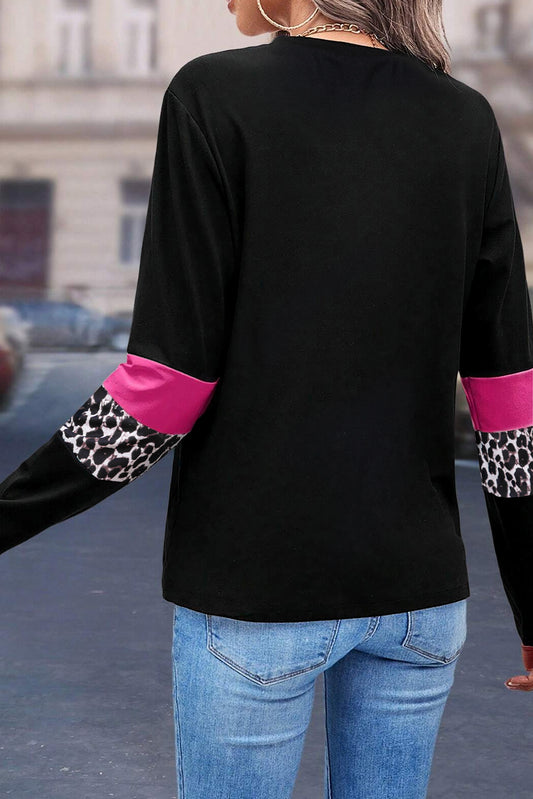 Person wearing a black long-sleeve top with pink and leopard print cuffs on a street.